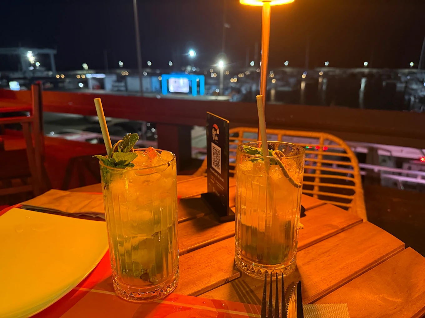 Dos cocktails con hierbabuena sobre mesa de madera frente a la marina de noche