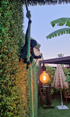 Figura de mono sobre una cuerda entre vegetación y bombillas cálidas en la terraza
